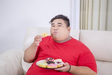 Şişman adam kanepede bir tabak çörek keyfi