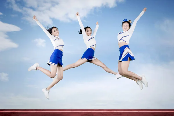 High school cheerleaders jumping with blue sky