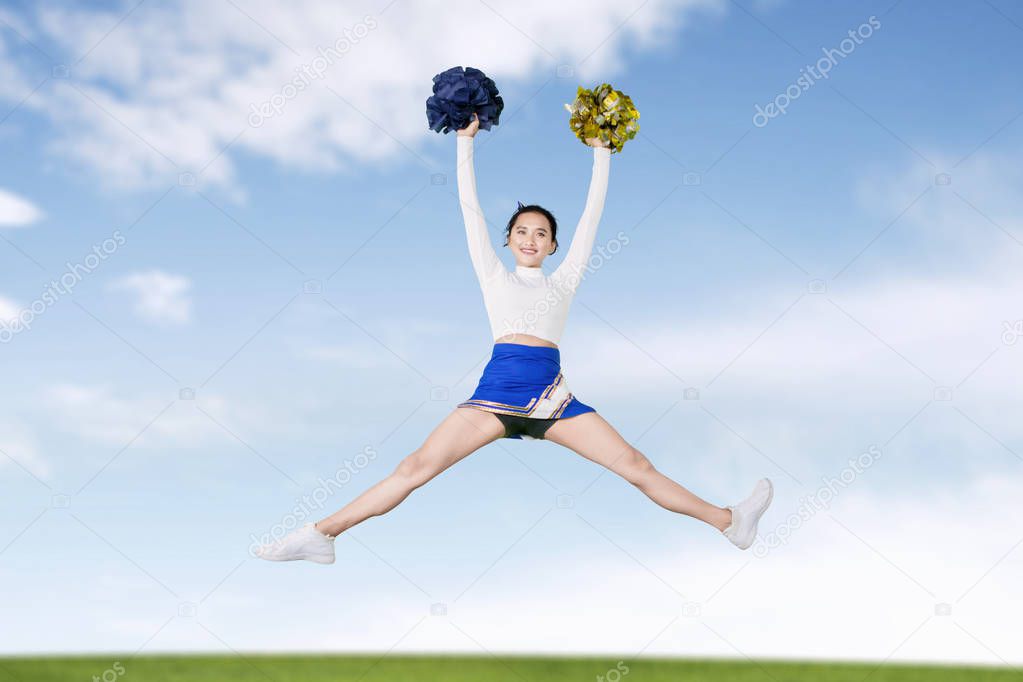Cheerleader girl jumps with pom poms in meadow