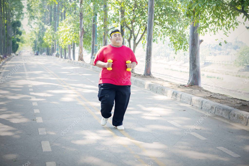Overweight man jogging with dumbbells in the park
