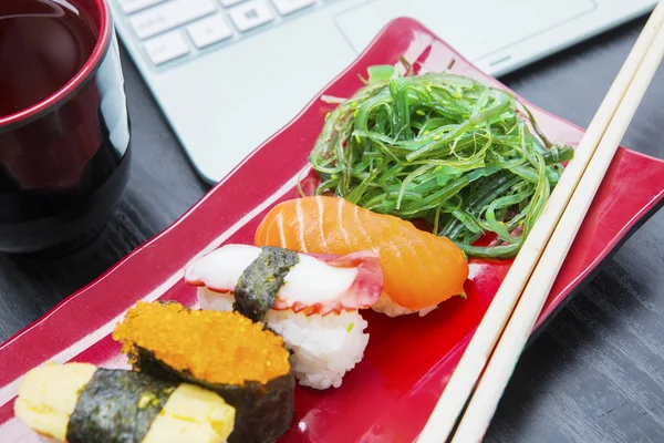 Sabroso sushi con portátil en la mesa — Foto de Stock