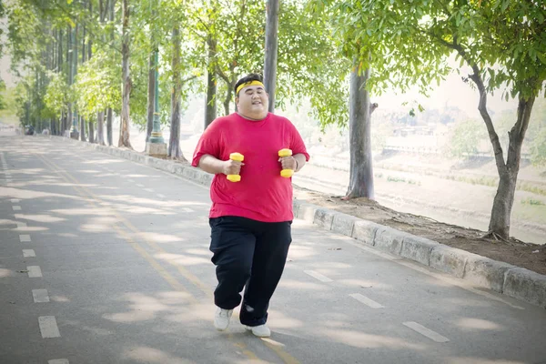Młody gruby człowiek jogging z hantlami na drodze — Zdjęcie stockowe