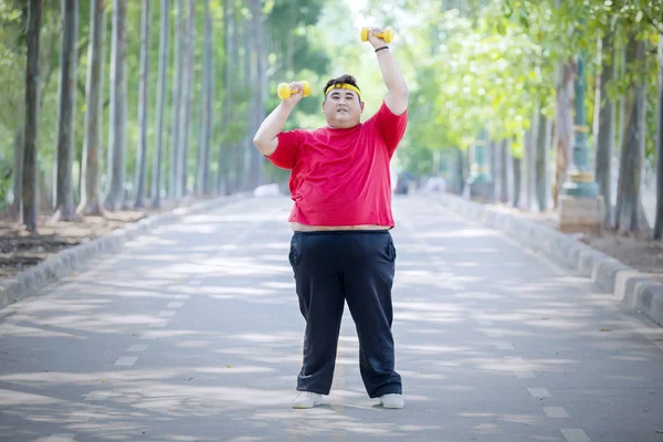 Young fat man lifting dumbbells on the road — Stock Photo, Image