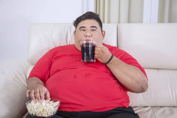 Молодой толстяк смотрит телевизор с колой и попкорном — стоковое фото