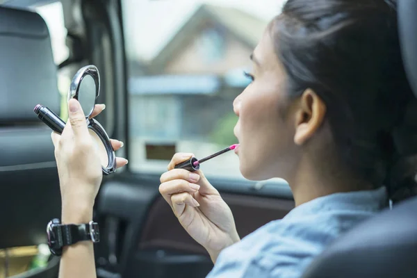 Mujer joven aplicando lápiz labial en sus labios en el coche — Foto de Stock