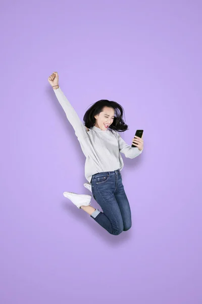 Mladá žena používá telefon a skáče ve studiu — Stock fotografie