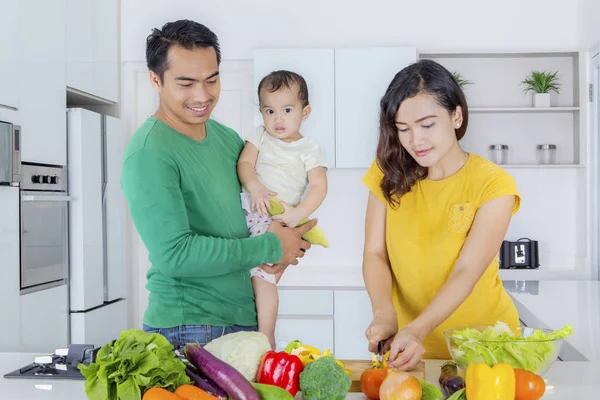 Mother prepares salad with her husband and baby — Stock Photo, Image