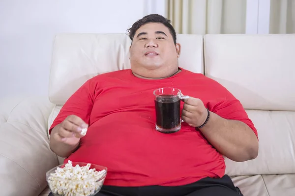 Obézní muž, který se dívá na televizi s colou a popcorn — Stock fotografie