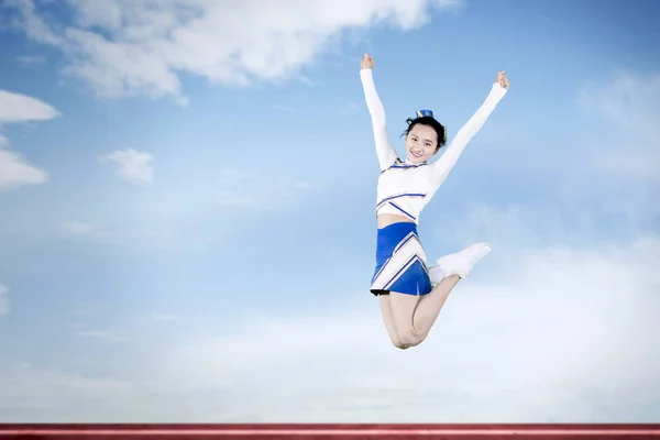 かわいいチアリーダーは、青い空の背景でジャンプ — ストック写真