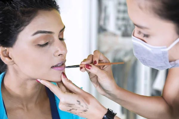 化妆艺术家在化妆室用刷子在她的模特唇上涂口红的图片 — 图库照片