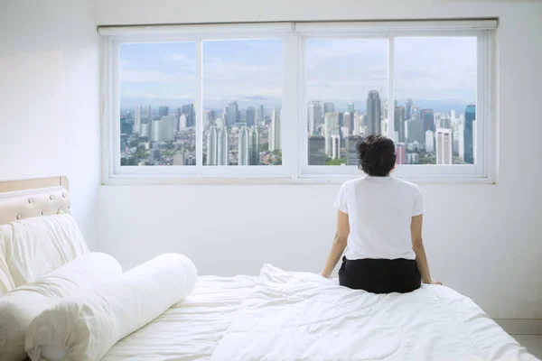 Vrouw kijkt naar het stadslandschap in het raam van het appartement — Stockfoto