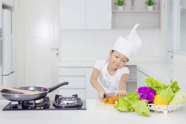 Süßes kleines Mädchen schneidet eine Möhre in der Küche — Stockfoto