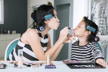 Anne çocuğunun dudaklarına ruj sürüyor.