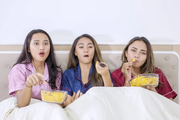 Güzel genç kızlar yemek yer ve yatakta televizyon izlerler. — Stok fotoğraf