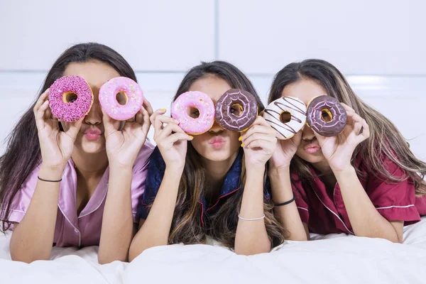 Grupo de meninas cobre os olhos com donuts na cama — Fotografia de Stock