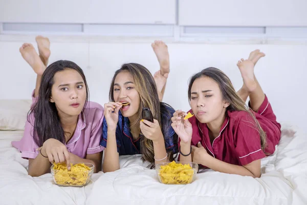 Groep van tienermeisjes eet en kijkt TV in bed — Stockfoto