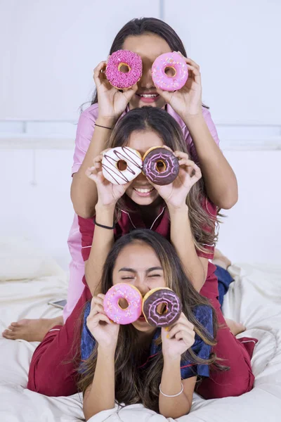 Teenage girls covering their eyes with donuts in bed