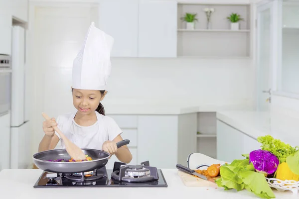 Malá holka dělá míchat smaženou zeleninu v kuchyni — Stock fotografie