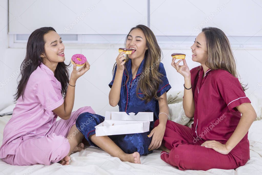 Happy teenage girls eating donuts in bed