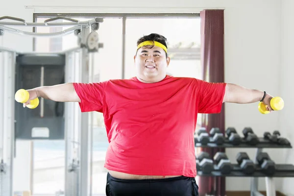 Jeune homme gras tient deux haltères dans le centre de gym — Photo