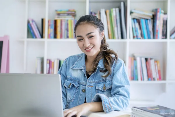 Mosolygó tizenéves lány tanul laptop a könyvtárban — Stock Fotó