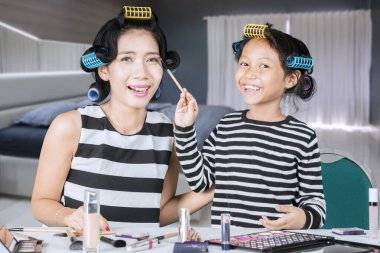 Küçük mutlu kız annesine rimel sürüyor.