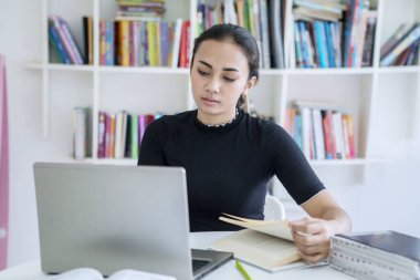Kütüphanede dizüstü bilgisayar kullanan Asyalı genç kız.