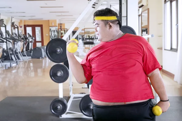 Young obese man with dumbbells in gym center — Stock Photo, Image