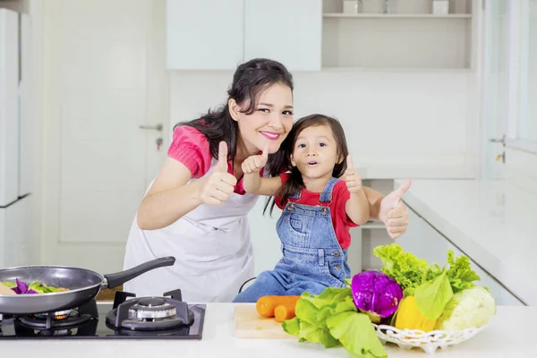 Женщина и ребенок показывают большие пальцы на кухне — стоковое фото