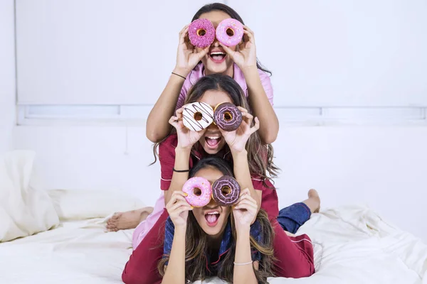Ευτυχισμένα κορίτσια καλύπτουν τα μάτια τους με ντόνατς στο κρεβάτι — Φωτογραφία Αρχείου