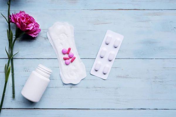 Almohadilla menstrual con pastillas y rosas sobre mesa de madera — Foto de Stock