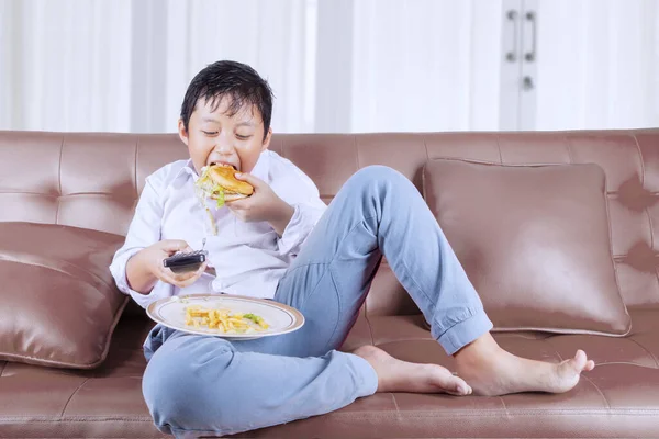 Menino obeso assistindo TV e comendo junk foods — Fotografia de Stock