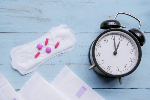 Pastillas y toallas sanitarias con despertador en la mesa — Foto de Stock