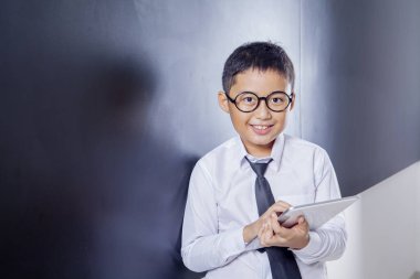 Gülümseyen okul çocuğu sınıfta bir tablet tutuyor.