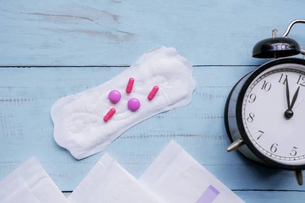 Almohadillas sanitarias con píldoras y despertador en la mesa — Foto de Stock