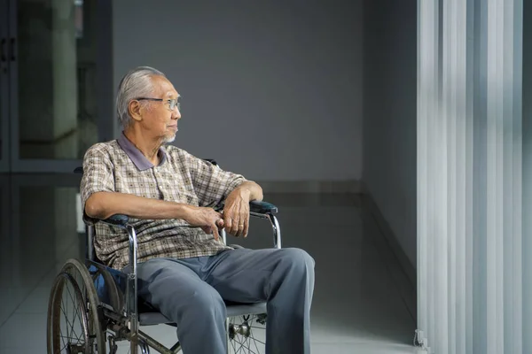Un aîné est assis dans un fauteuil roulant près de la fenêtre — Photo