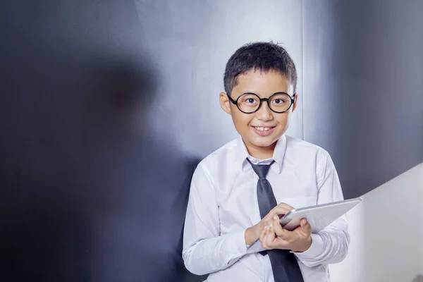 Escolar sonriente sostiene una tableta en el aula — Foto de Stock