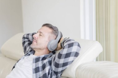 Kafkasyalı bir adam kanepeye oturmuş kulaklıklarıyla dinleniyor.
