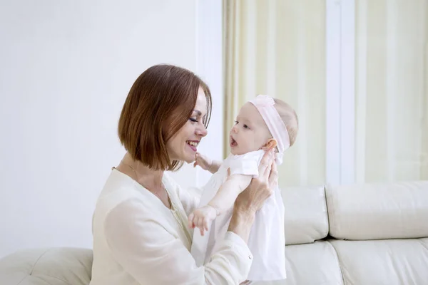 Junge Frau hält ihr süßes Baby auf der Couch — Stockfoto