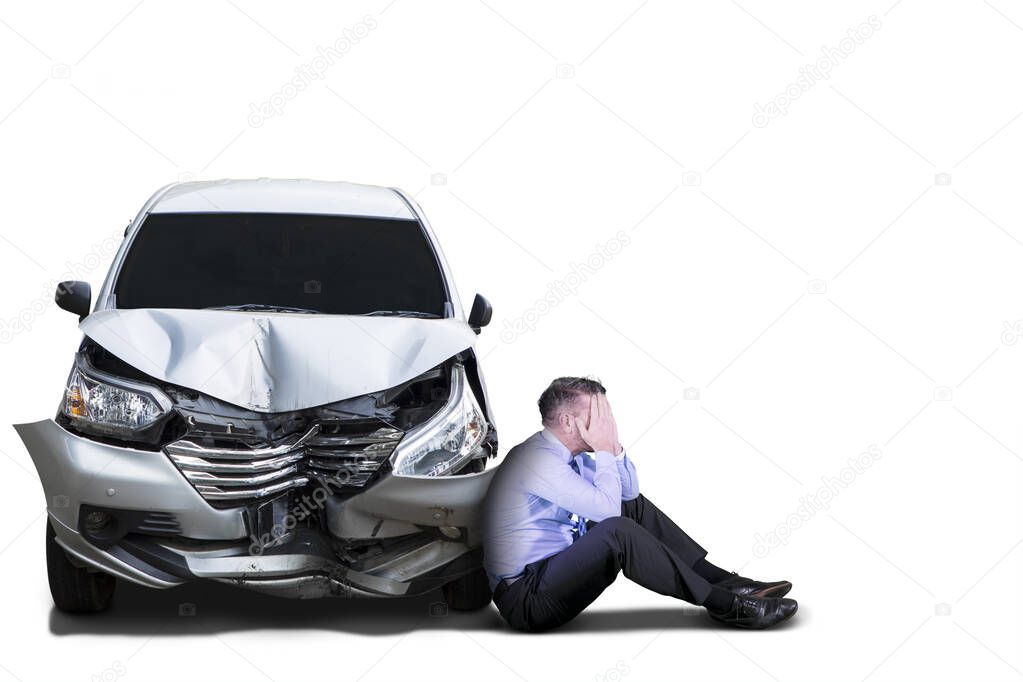 Depressed businessman sitting near a damaged car