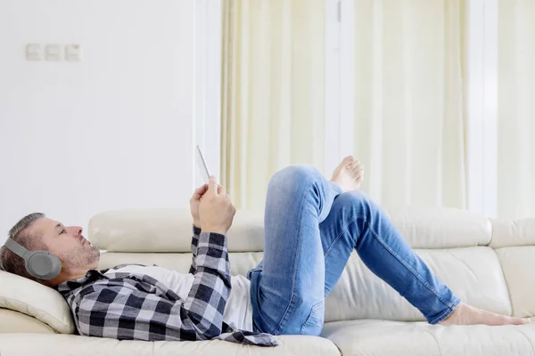 Kaukasischer Mann liegt auf Couch und genießt Musik — Stockfoto