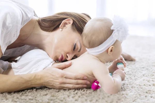 Caucasian woman kissing her baby on the carpet — Stock Photo, Image