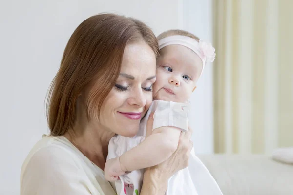 Cute baby in a tender embrace of mother on couch — Stock Photo, Image