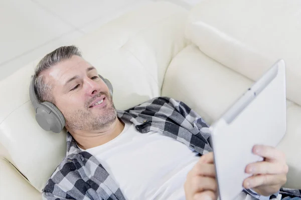 Happy man enjoying music with a tablet on couch — Stock fotografie