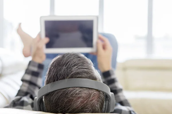 Muž ležící na gauči, zatímco si užívá hudbu s tabletem — Stock fotografie