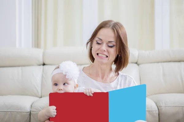 Shocked mother looking her baby girl bites a book — ストック写真
