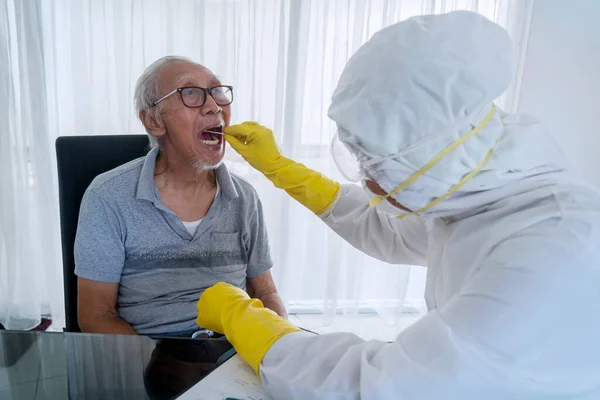 与穿着防护服的医护人员一起做包扎测试的年长男子 以抽取肠病毒爆发样本 — 图库照片