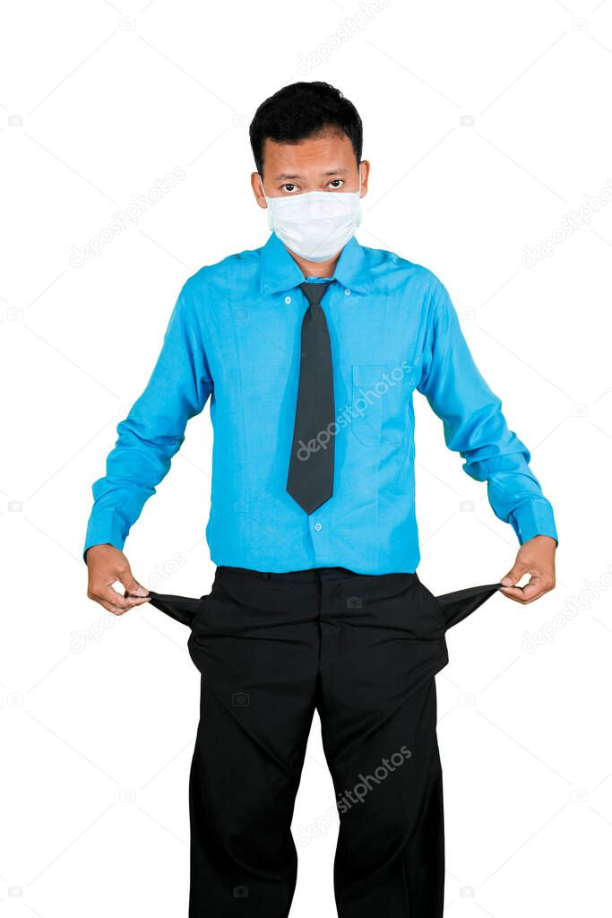 Young businessman wearing medical mask and showing empty pocket in the studio, isolated on white background. Coronavirus outbreak impact concept