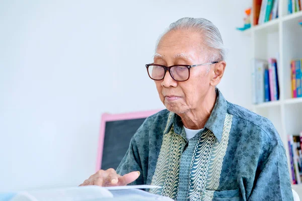 Close up of old man wearing glasses while enjoying leisure time with reading a textbook in the library