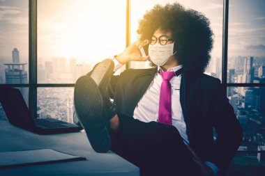 Ofiste dizüstü bilgisayarı ve ayağı masada otururken erkek müdür cep telefonuyla konuşuyor.